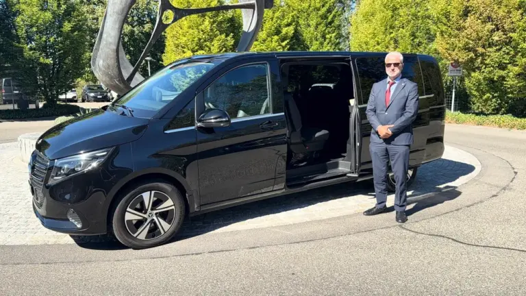 Chauffeur neben einer schwarzen Mercedes V-Klasse mit geöffneter Schiebetür